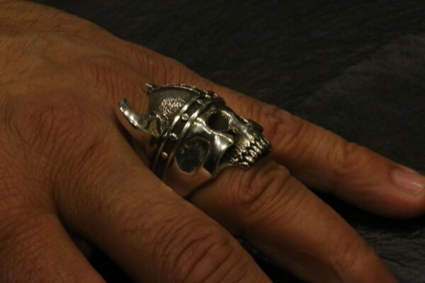 A silver skull ring worn on a finger against a dark background.