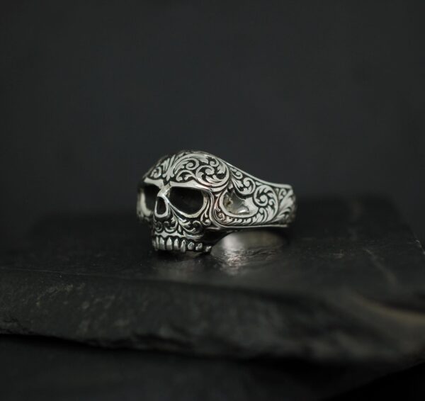 Intricately designed silver skull ring with ornate patterns.