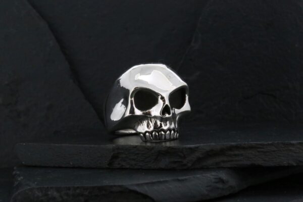 A shiny silver skull ring on a dark surface.