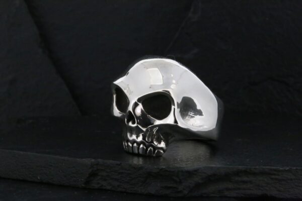 A shiny silver skull ring on a dark surface.