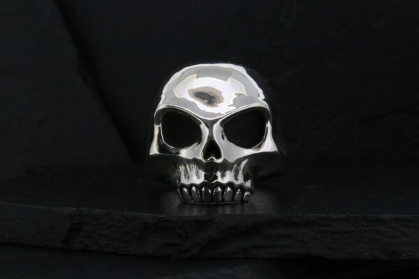 A silver skull ring on a black surface.