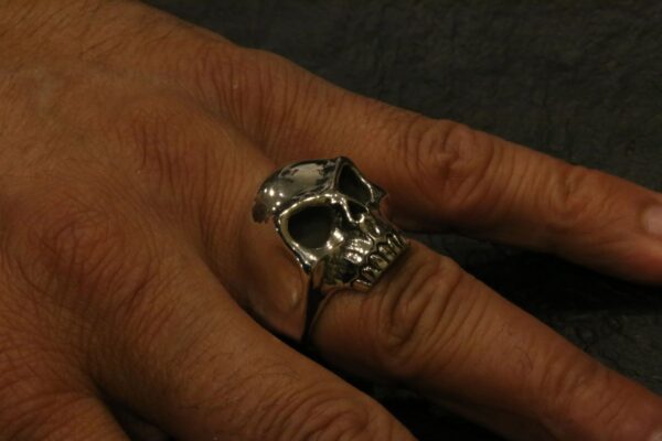 A hand wearing a silver skull-shaped ring.