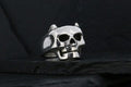 A metallic skull ring with intricate details on a dark background.