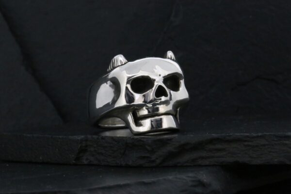 A metallic skull ring with intricate details on a dark background.