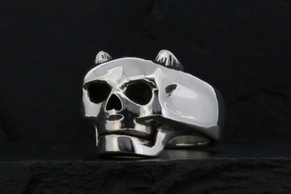 A silver skull ring with a pipe on a black background.
