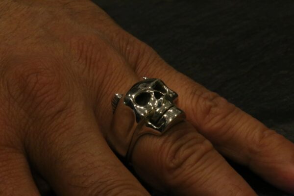 A hand wearing a silver skull ring on the finger.