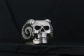 A silver skull with ram horns against a dark background.
