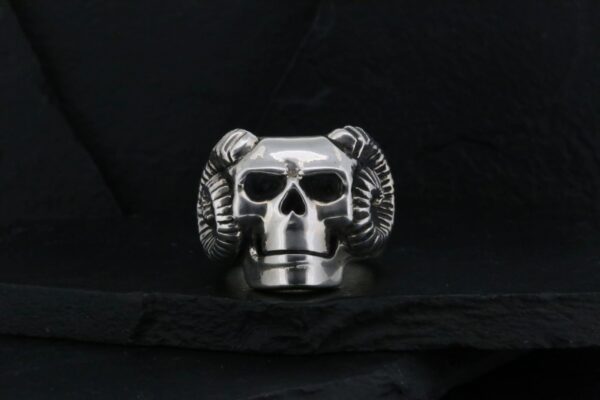 Silver skull ring with ram horns on black background.