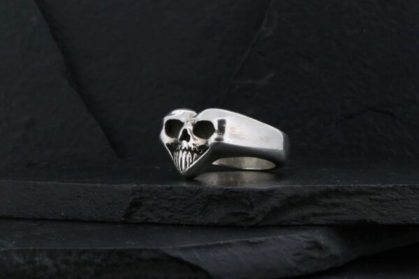 Silver ring with a skull design on a dark background.