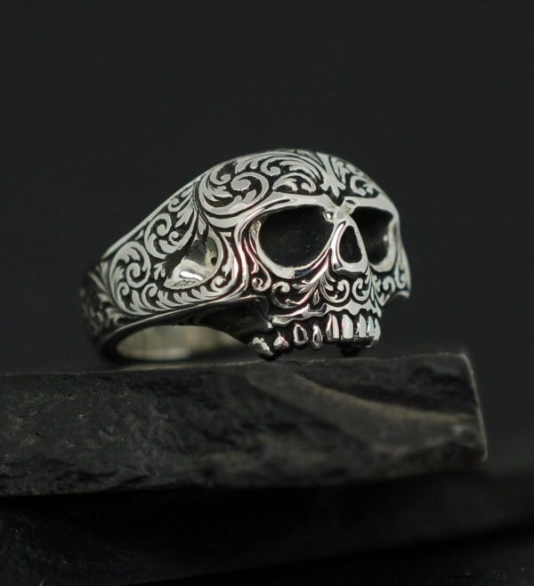 Intricately carved silver skull ring with floral patterns.