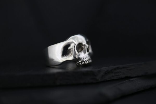 A silver skull-shaped ring on a black surface.