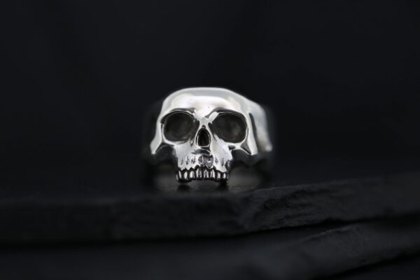 A metallic skull ring on a dark surface.