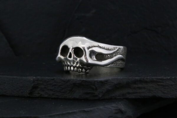 A silver ring shaped like a detailed skull on a dark surface.