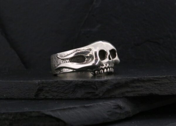 A silver skull ring with intricate details on a dark background.
