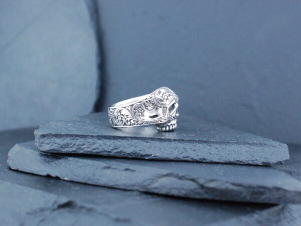 Close-up of an intricately designed silver ring on a textured blue surface.