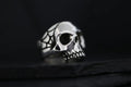 A silver skull ring with spider web details on a dark background.