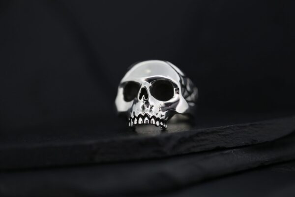 Close-up of a silver skull-shaped ring on a dark surface.