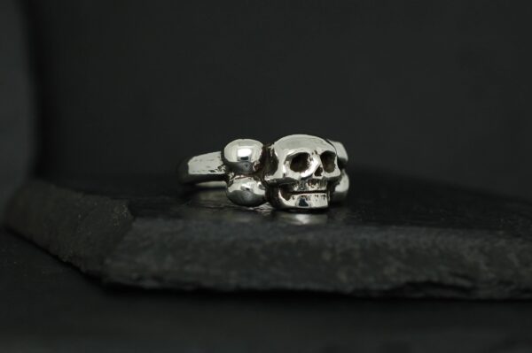 Two silver skull rings on a dark surface.