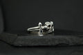 Silver ring featuring a skull and dagger design on a dark background.