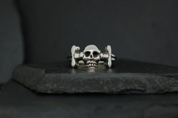 A silver skull ring on a dark stone surface.