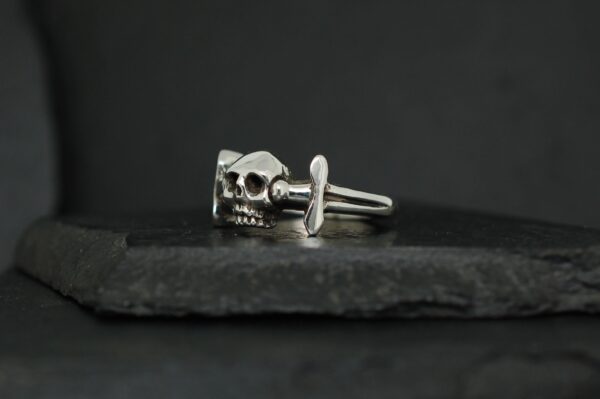 Silver skull ring with intricate details on a dark surface.