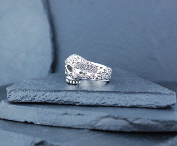 Elegant silver ring with intricate design on stone surface.