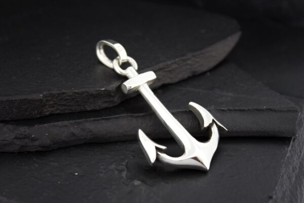 Silver anchor pendant on a dark surface.