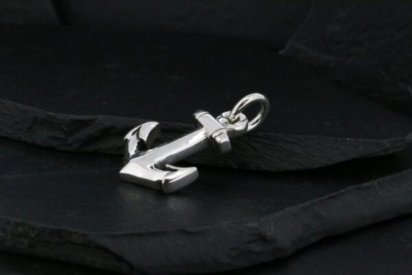 A silver anchor pendant on a black fabric background.