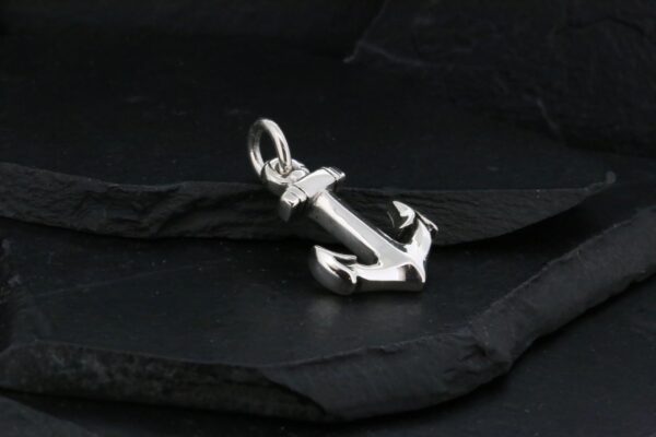 A silver anchor pendant on a dark surface.