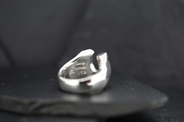 Close-up of a silver ring with unique cut-out design on a dark background.