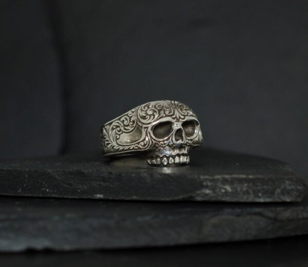 A silver skull ring on a dark textured surface.