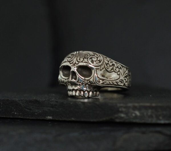 Intricately detailed skull ring with floral engravings on a dark background.