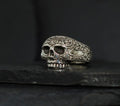 Intricately detailed skull ring with floral engravings on a dark background.