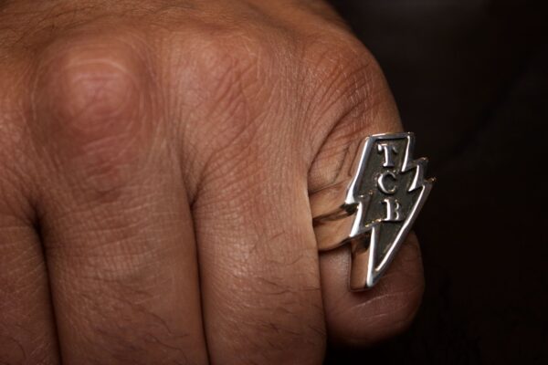 Close-up of a hand wearing a silver ring with the word 'FUCK' and a lightning bolt.