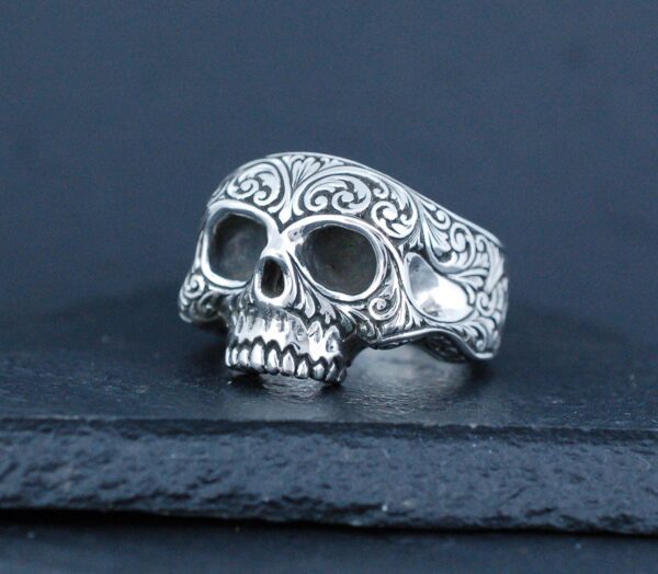Intricately designed silver skull ring with ornate patterns.