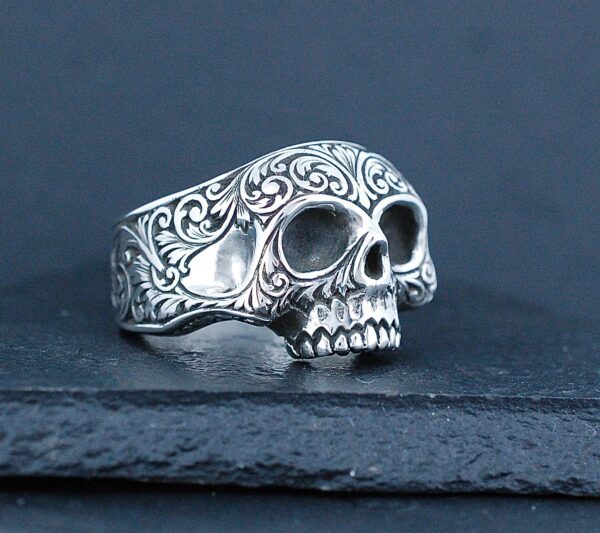 Intricately designed silver skull ring with ornate patterns.