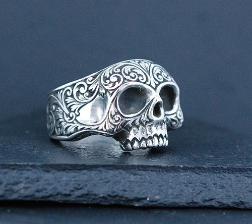 Intricately designed silver skull ring with ornate patterns.