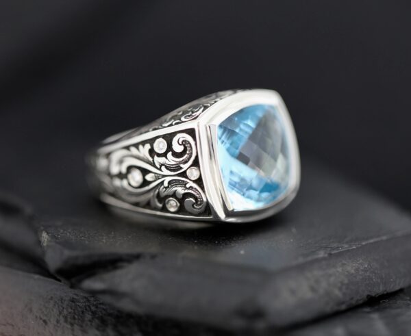 Elegant silver ring with intricate designs and a blue gemstone.