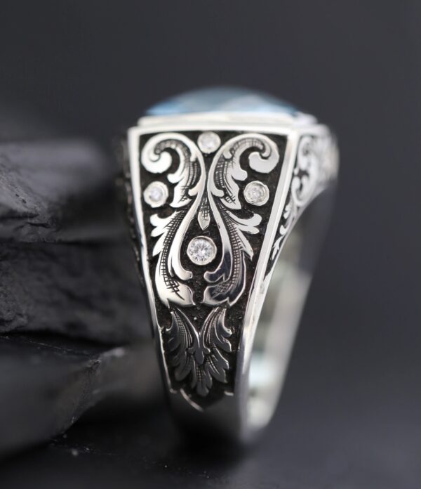 Close-up of an intricately engraved silver ring with floral patterns.