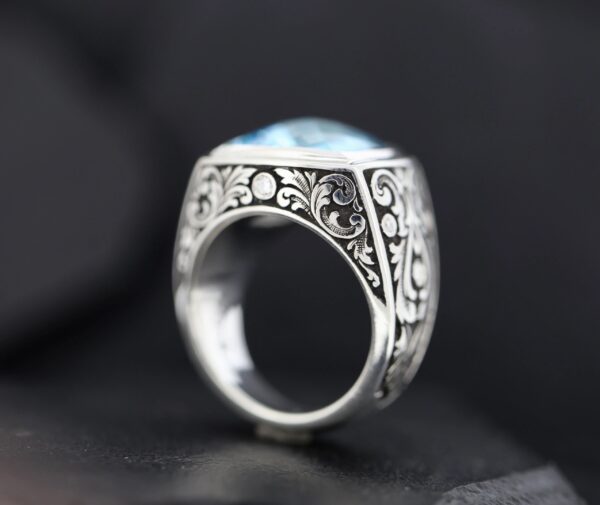 Close-up of an ornate silver ring with intricate floral engravings and a blue gemstone.