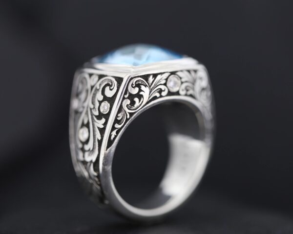 Ornate silver ring with intricate floral engravings and a blue gemstone.