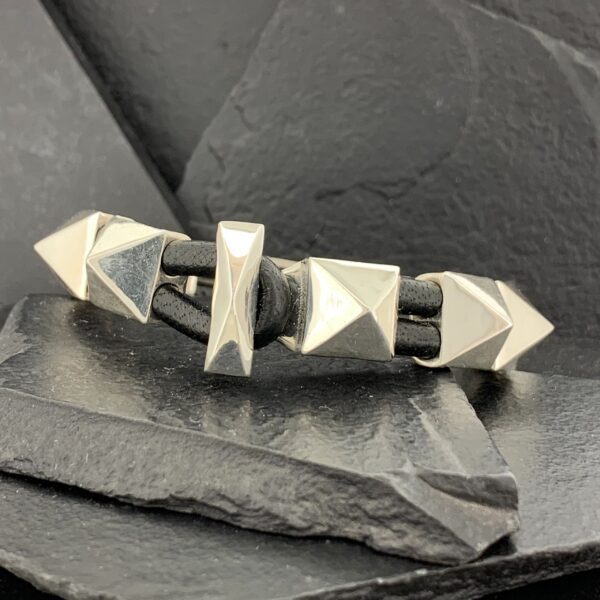 Silver ring with pyramid studs on a dark stone surface.