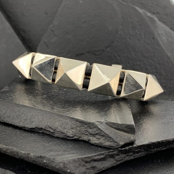 Silver geometric bracelet with pyramid shapes on a dark stone surface.