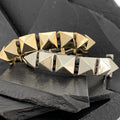 Two pyramid-studded bracelets in gold and silver tones on black slate.