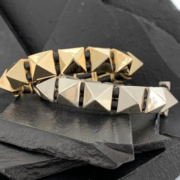 Two pyramid-studded bracelets in gold and silver tones on black slate.