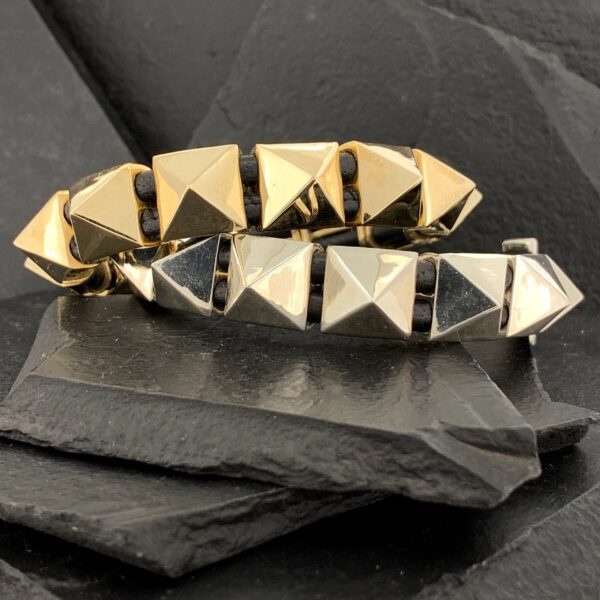 Two pyramid-studded bracelets, one gold and one silver, on black slate.
