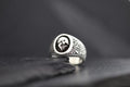 Silver ring with a skull emblem on a dark surface.