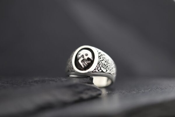 Silver ring with a skull emblem on a dark surface.