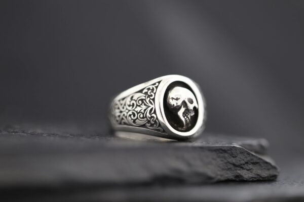 A detailed silver ring with a skull design on a black background.