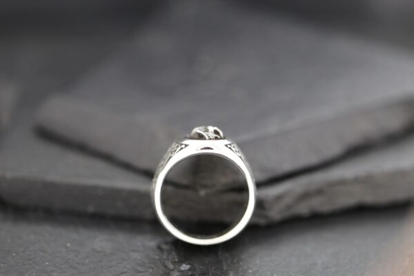 Close-up of a silver ring with a detailed design on a dark surface.